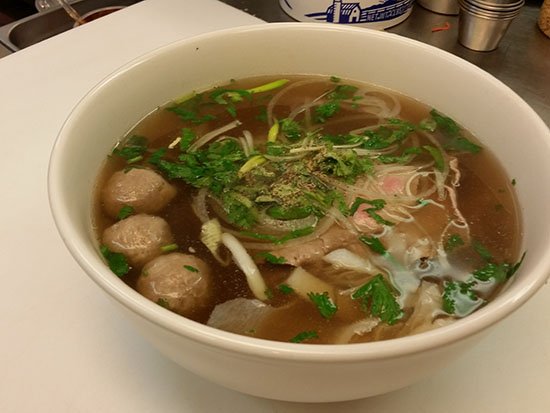 A bowl of Pho Lucky beef phở with rice noodles and fresh herbs